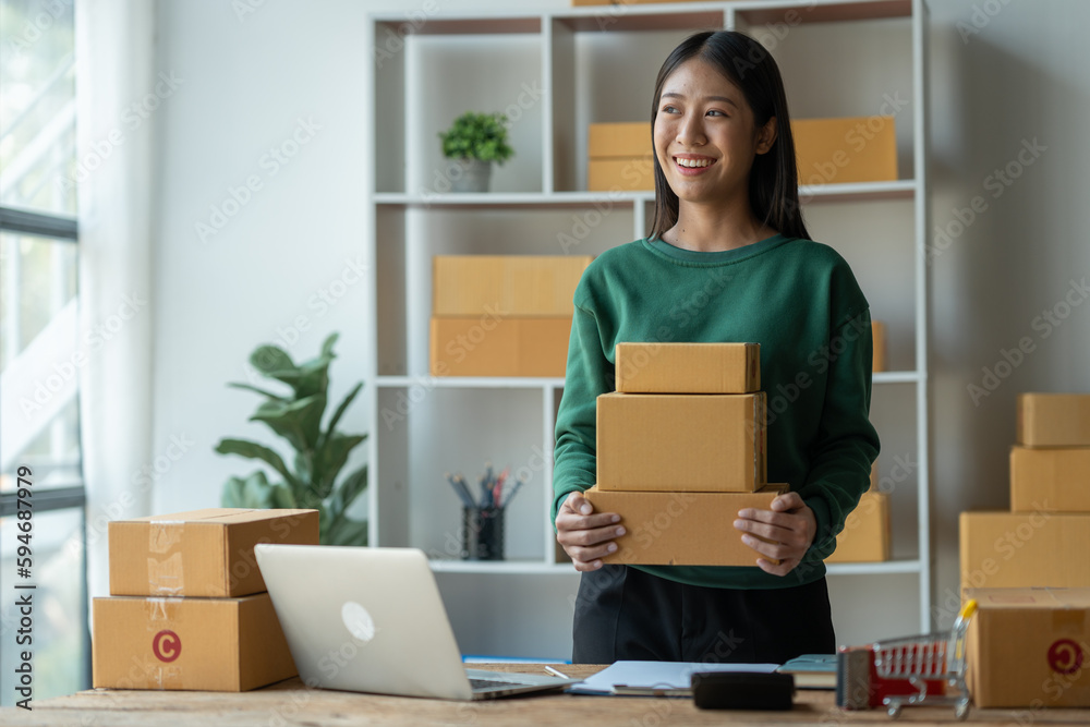 Asian female startup business owner She is smiling happily holding a box of parcels of customer orders that have been prepared to be delivered through the courier company online business selling idea Asian female startup business owner She is smiling happily holding a box of parcels of customer orders that have been prepared to be delivered through the courier company online business selling idea