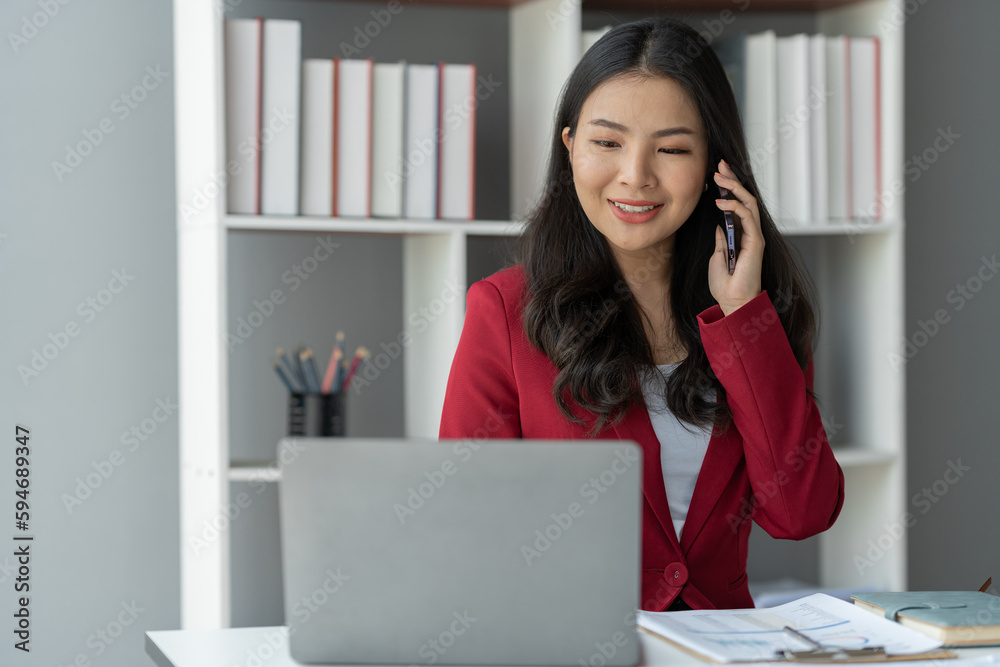 Pretty smiling asian businesswoman using mobile phone to view financial business data and communicate with customers viewing database. contract details appointment date and time on laptop in office Pretty smiling asian businesswoman using mobile phone to view financial business data and communicate with customers viewing database. contract details appointment date and time on laptop in office