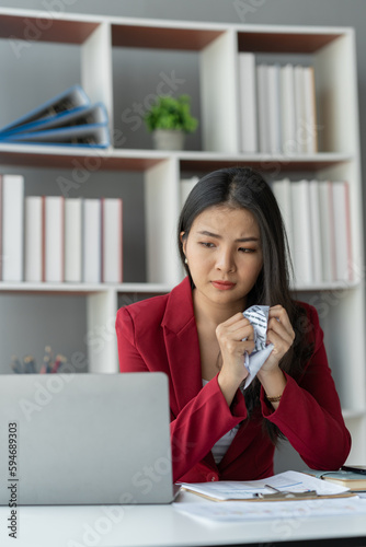 Tired and stressed Asian businesswoman with troubled paperwork With inaccurate information on her laptop, she crumpled the paper angrily from sitting the table a long time and have office syndrome