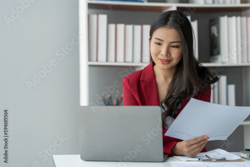 Smiling Asian businesswoman working on financial documents Contract details, taxes, preparation, gathering information before attending meetings within the office. © crizzystudio