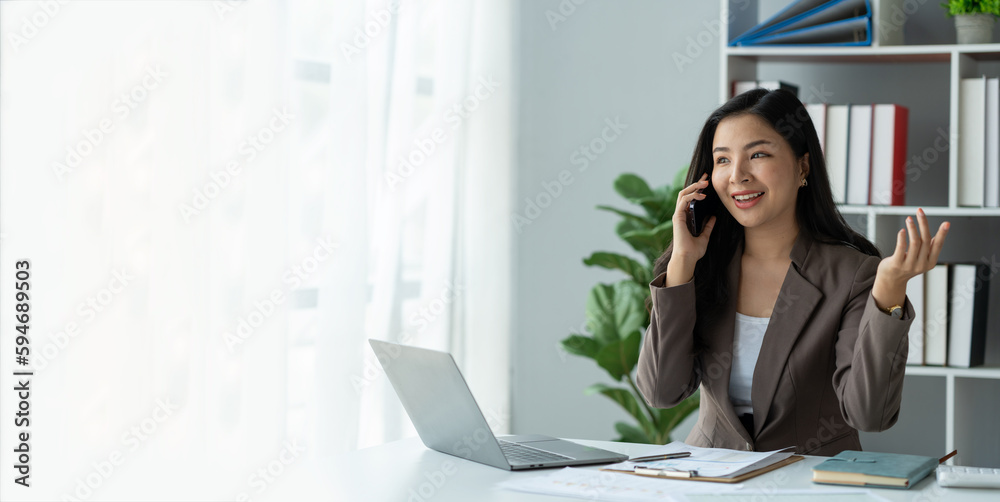 copy space, panorama ,banner , Happy young asian woman talking on the mobile phone and smiling while sitting at her working place in office. copy space, panorama ,banner , Happy young asian woman talking on the mobile phone and smiling while sitting at her working place in office.