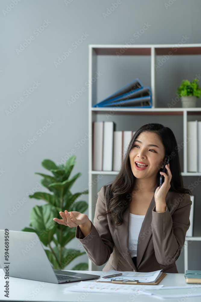 Happy young asian woman talking on the mobile phone and smiling while sitting at her working place in office. Happy young asian woman talking on the mobile phone and smiling while sitting at her working place in office.