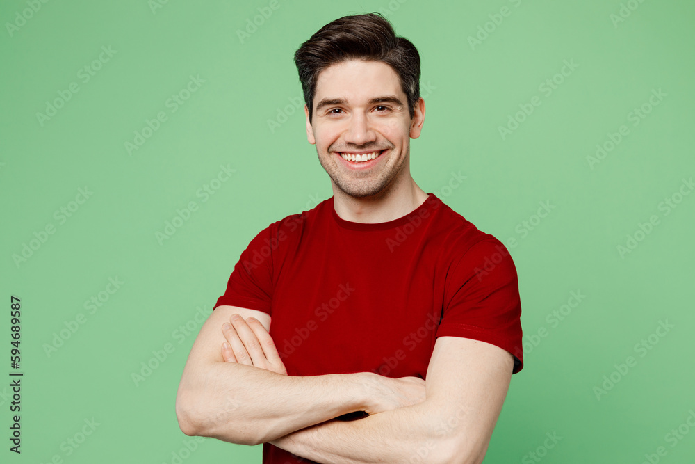 Young smiling cheerful brunet confident man he wears red t-shirt casual clothes look camera hold hands crossed folded isolated on plain pastel light green background studio portrait Lifestyle concept Young smiling cheerful brunet confident man he wears red t-shirt casual clothes look camera hold hands crossed folded isolated on plain pastel light green background studio portrait Lifestyle concept