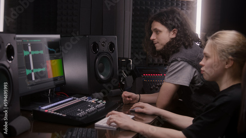 Female audio engineer and musician create song in music recording room. Computer screen showing DAW software interface with sound track. Modern equipment in sound recording studio. Music production.