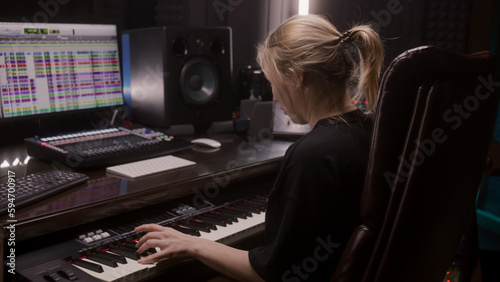 Female sound engineer, musician uses MIDI controller, digital electric piano for creating music. Computer screen shows DAW software interface with sound tracks. Recording studio. Music production.