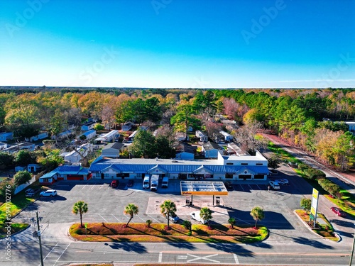 Aerial view of a parking lot of a building surrounded by tall trees under a clear blue sky.
