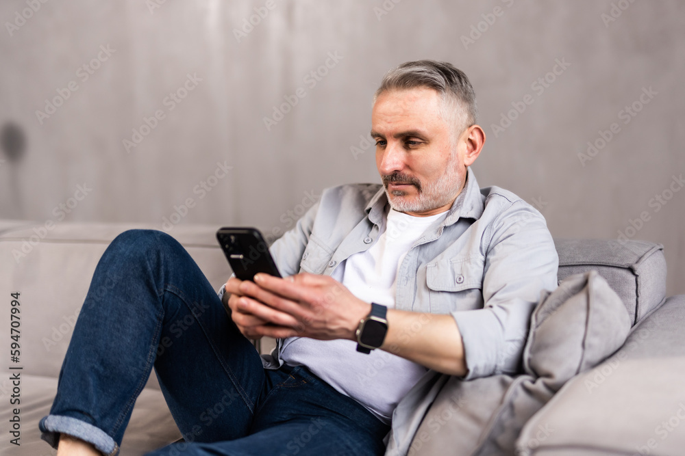 Older man at home, sitting on couch in living room, using phone, checking social media.