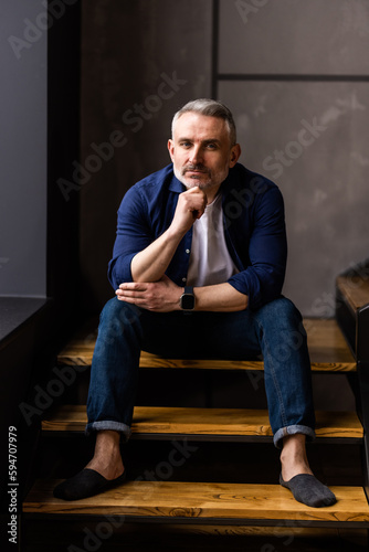 Mature middle age man sitting on stairs at home