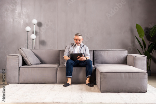 Attractive man relaxing on a sofa with a tablet-pc reading or watching media with a quiet smile