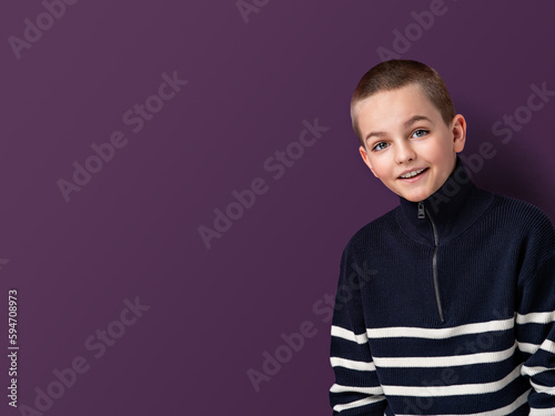 A photo of a young boy with short haircut and cozy sweater showing childish curiosity and positivity in his facial expression. Teenager looking friendly and confidently. Background with copy space.