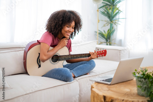 African American young woman thinking and choosing music cord using laptop to play guitar as her lifestyle on weekend, holiday, Black girl plactice music in strument.