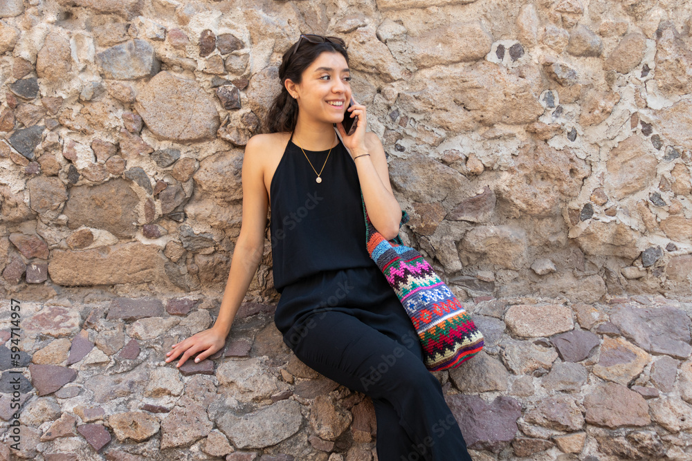 Cheerful woman talking on smartphone while sitting on stone wall Cheerful woman talking on smartphone while sitting on stone wall