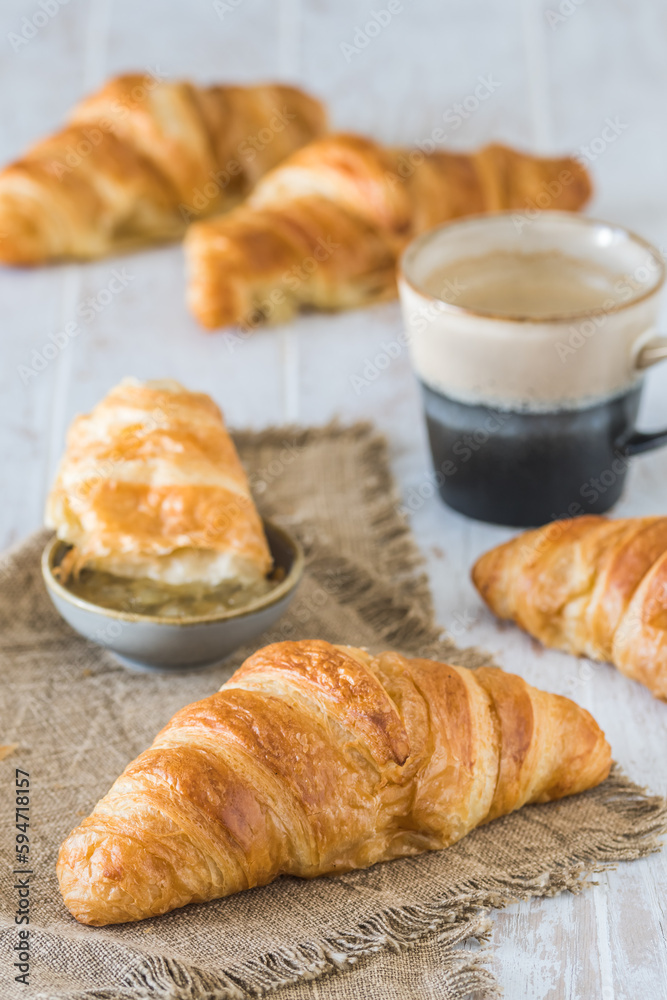 Delicious French croissant on a white wooden table, a cup of coffee and croissants in the background, breakfast scene, vertical