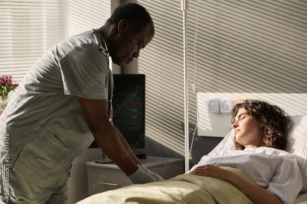 Obraz premium African American doctor making dropper for young patient while she sleeping on bed in ward