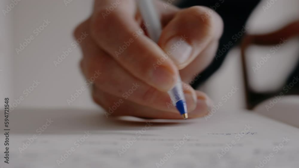 A man writes a text on a sheet with a blue pen. Man makes notes in a notebook. The student writes a lecture note.
