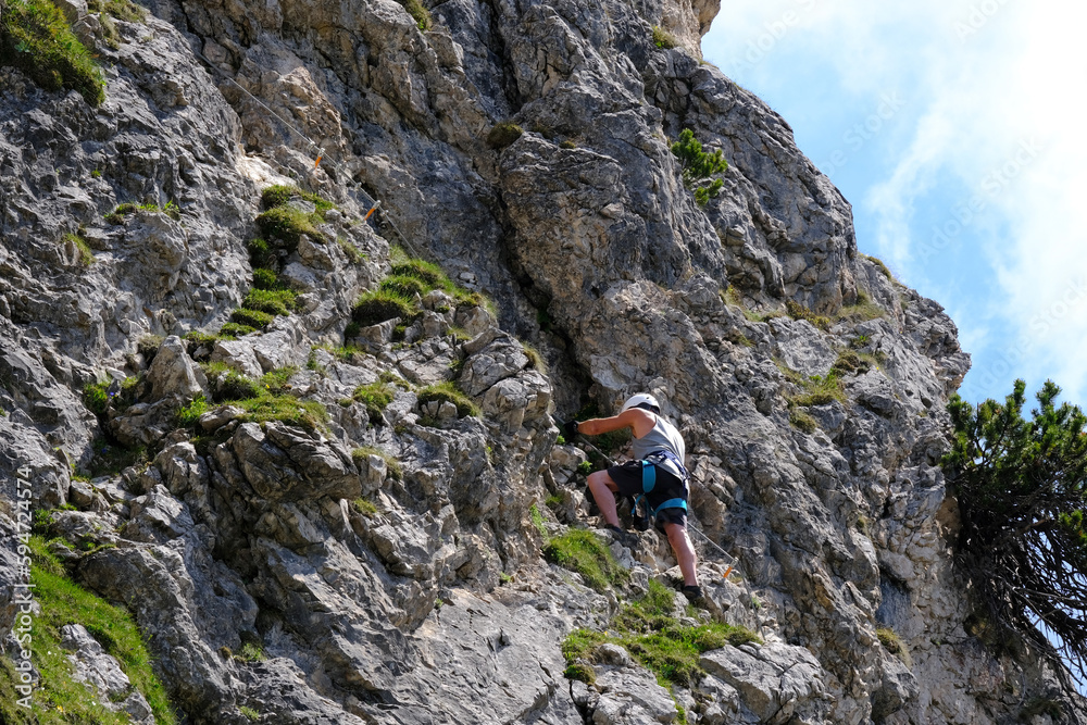 man in body harnesses feature life-safety, attaches hooks to iron brackets, climbs rock, active lifestyle of people, mountaineering, via ferrata in mountains of alps, life insurance in extreme sports