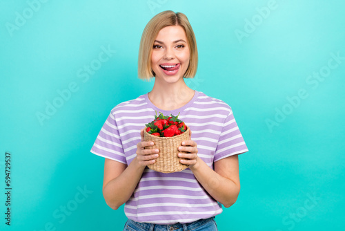 Photo of satisfied woman bob hairdo dressed striped t-shirt hold basket of strawberries tongue lick lips isolated on teal color background