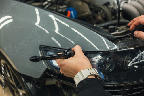 The process of installing a protective polyurethane film for paint on the front headlight of a car. PPF is a polyurethane film that helps protect glass and metal from scratches. Selective focus.   © Dmitry Presnyakov