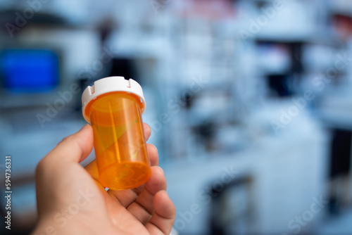 Hand holding an empty orange bottle of medicine in laboratory background