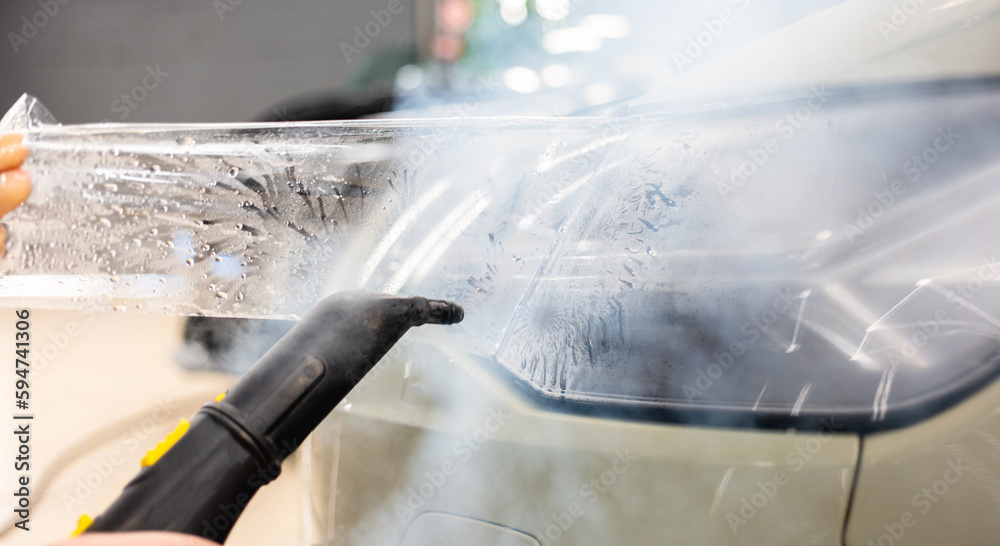 The process of installing a protective polyurethane film for paint on the front headlight of a car. PPF is a polyurethane film that helps protect glass and metal from scratches. Selective focus.  
