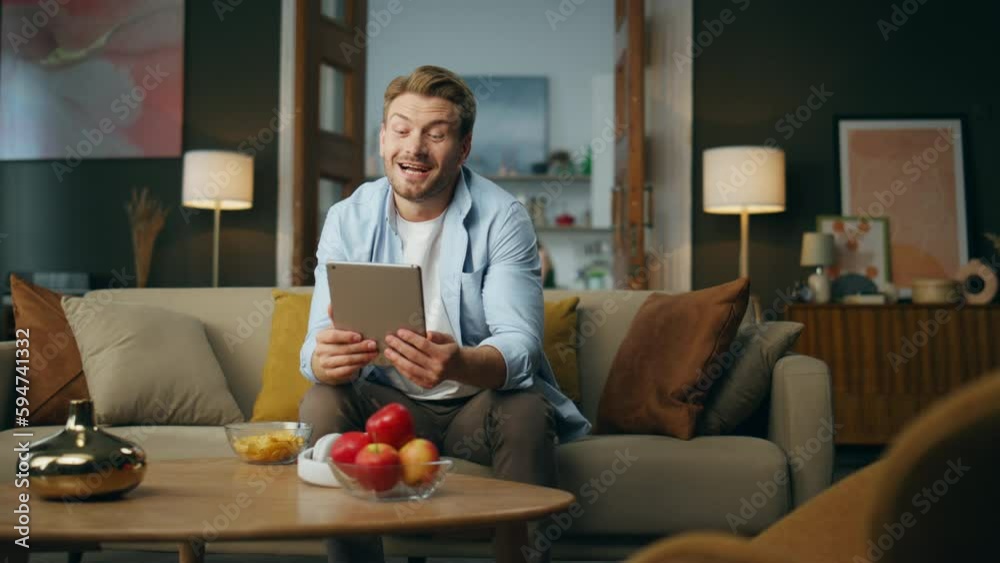 Friendly man waving hand speaking tablet computer at home. Relaxed guy sitting Friendly man waving hand speaking tablet computer at home. Relaxed guy sitting