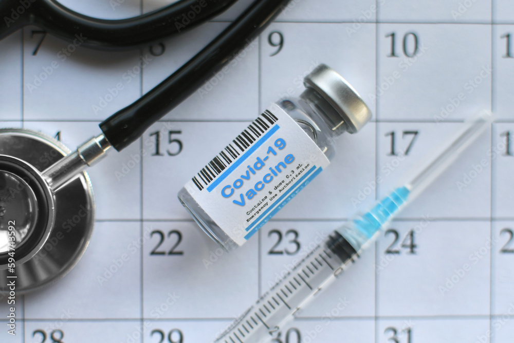 Scheduling Covid-19 vaccine & booster dose concept. Vial syringe stethoscope flat lay on calendar.