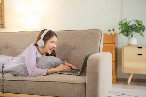 Happy young teenage beautiful Asian woman using tablet for home entertainment while sitting on the couch in the house.