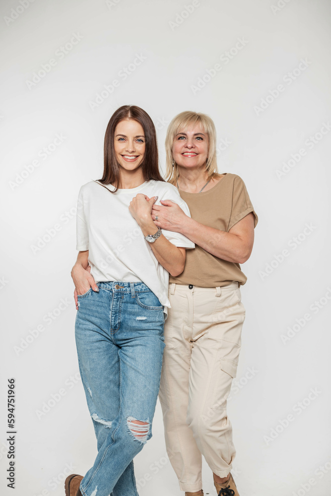 Beautiful young happy woman daughter and mom smiling in trendy fashion denim casual clothes with t-shirt on white background in studio Beautiful young happy woman daughter and mom smiling in trendy fashion denim casual clothes with t-shirt on white background in studio