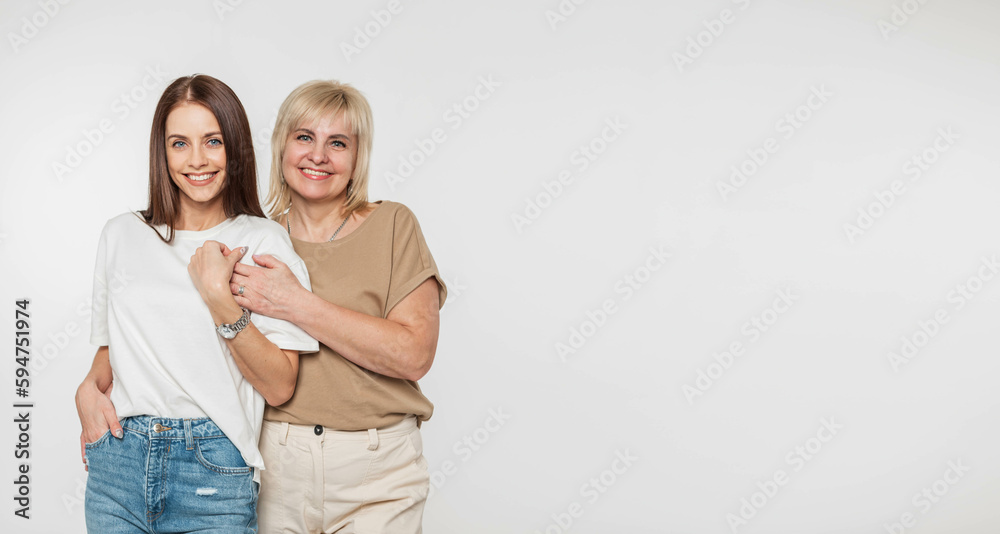 Beautiful happy mother and daughter in fashionable clothes with t-shirts and denim on a white background with copy free space for design and text. Pretty elderly woman hugging a beautiful young girl Beautiful happy mother and daughter in fashionable clothes with t-shirts and denim on a white background with copy free space for design and text. Pretty elderly woman hugging a beautiful young girl