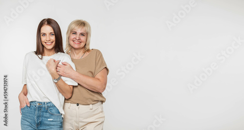 Beautiful happy mother and daughter in fashionable clothes with t-shirts and denim on a white background with copy free space for design and text. Pretty elderly woman hugging a beautiful young girl