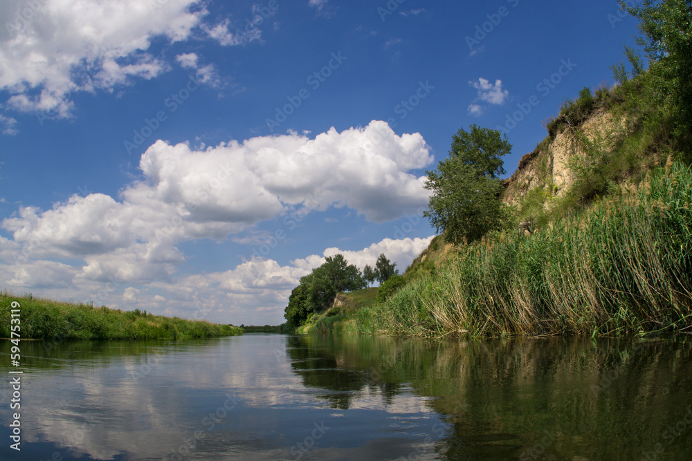 A riverbed with steep banks and a summer blue sky with cumulus clouds.