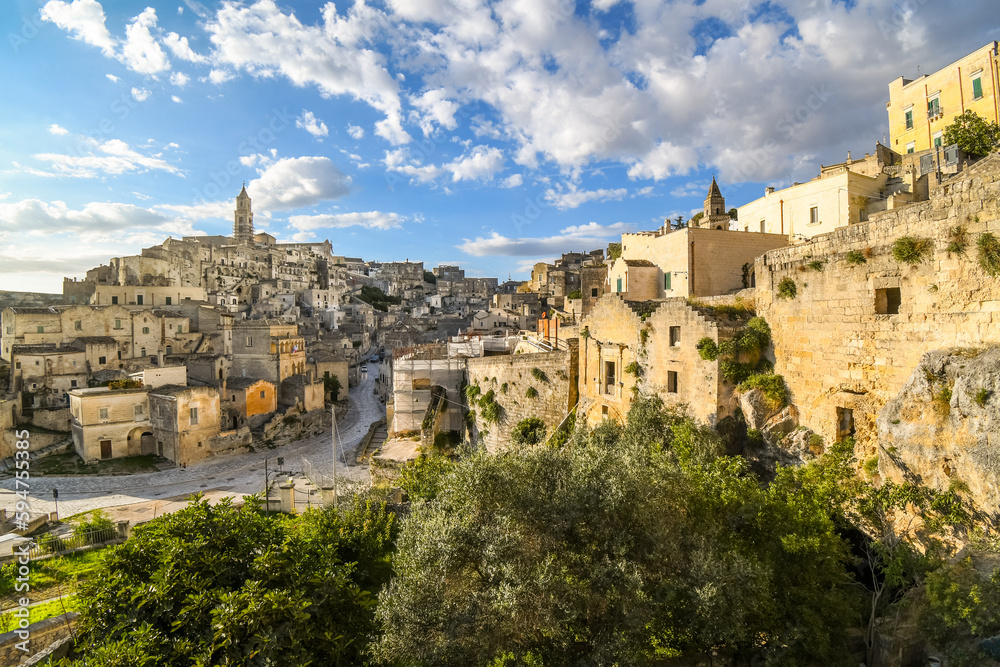 Hillside view of the ancient city of Matera, Italy in the Basilicata region, including the old town, tourist street and mountain path, Sasso Barisano tower and the steep ravine canyon below.