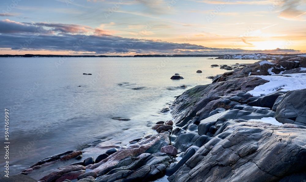 Stunning coastal shoreline, featuring a rocky shore and tranquil waters, with orange sunset