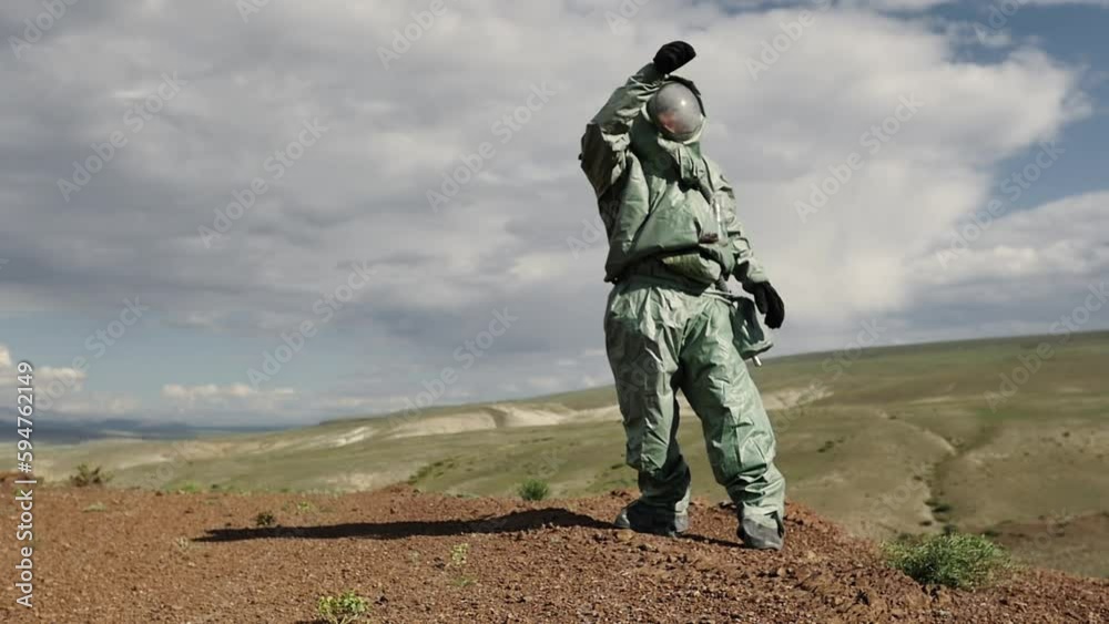 An ecologist, a biologist in a protective suit dropped and broke a test tube with material for research. Possibly in a toxic hazardous area with contaminated soil