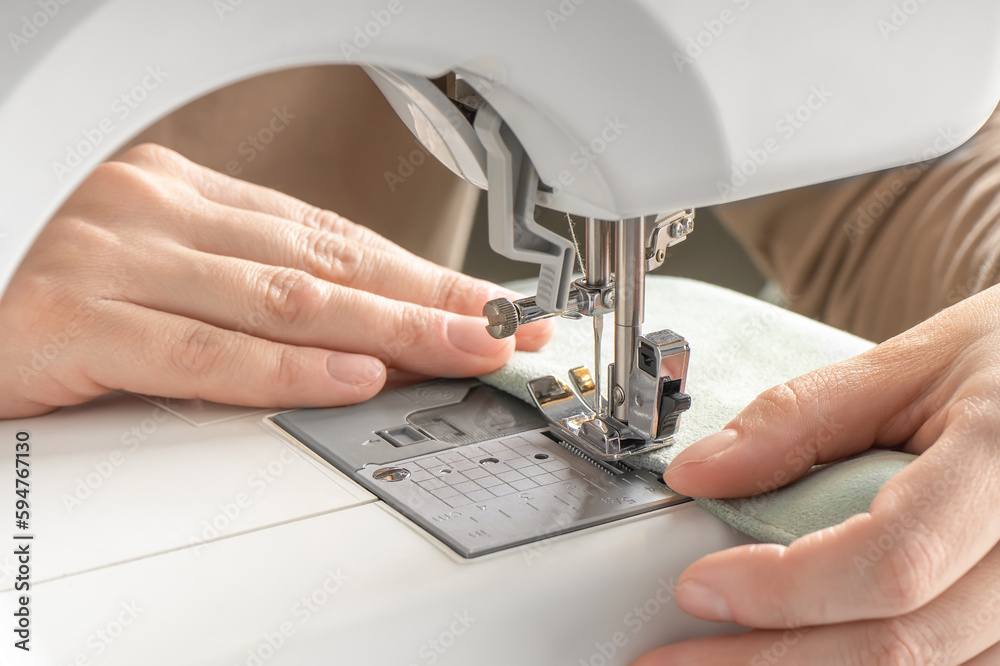 Female hands stitching white fabric on modern sewing machine at workplace in atelier
