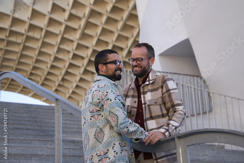 Real marriage of gay couple, holding hands, with a railing of a stairs in the middle of the two, happy and complicit. Concept lgtb, lgtbiq+, couples, in love, love. © Manuel