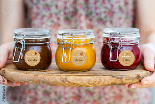 Closeup Foto: Marmeladen Gläser auf einer Holzplatte mit Aprikose, Erdbeere, Pflaume - eingemachtes Obst