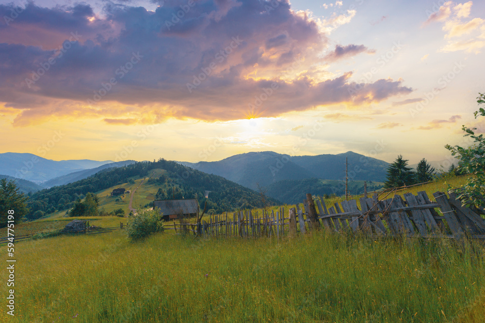 Idyllic rural scenery in the Carpathian mountains, Ukraine. An old wooden fence goes along the pathway on the high grass hill under the bright sunset sky.