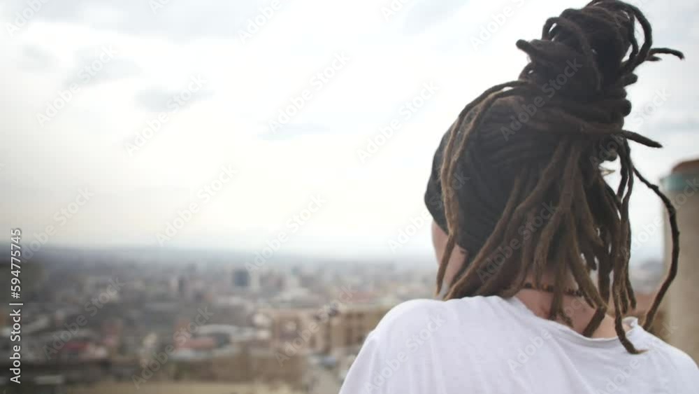 a lonely young man with dreadlocks gathered in a bun looks at the city from a high place. Looking behind. a young Brazilian man with dreadlocks and an earring in his ear looks at the city landscape a lonely young man with dreadlocks gathered in a bun looks at the city from a high place. Looking behind. a young Brazilian man with dreadlocks and an earring in his ear looks at the city landscape