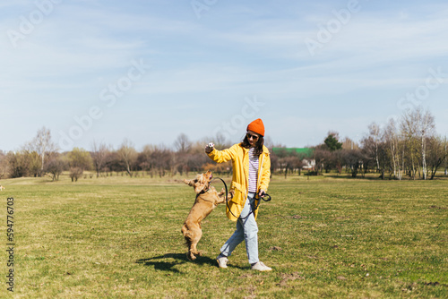  a girl in a yellow raincoat  a red hat and glasses walks with a spaniel dog in a park on the grass in sunny weather  trains and says command