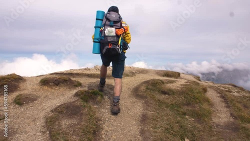 Young man hiker on mountain with cloudy sky and fog. Yellow jacket, backpack and beanie. Traveling Dolomites, Italy.