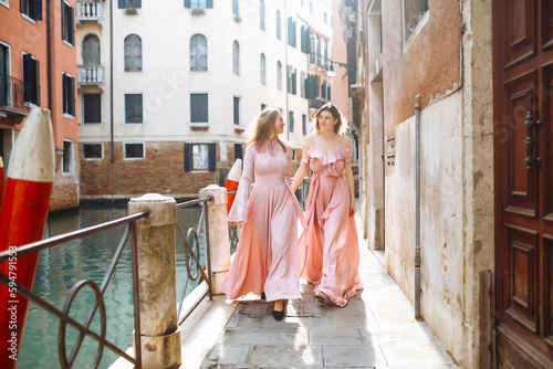 Beautiful mother and daughter are walking in sunny Venice in fashionable soft pink dresses. Daughter and mother enjoy city landscapes. Concept of an active lifestyle, travel, vacation.