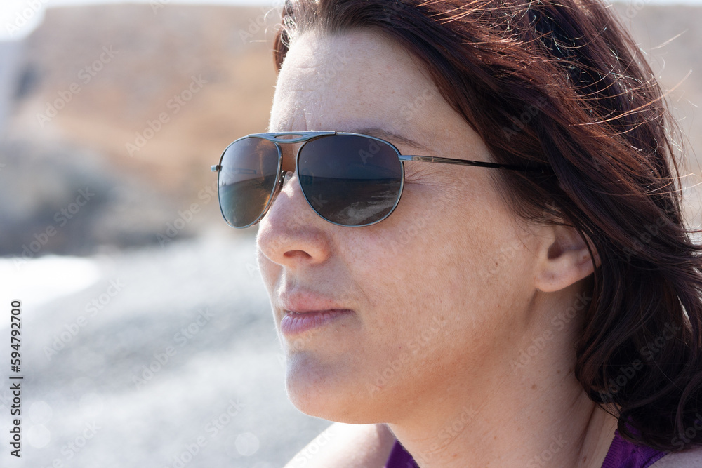 portrait of a woman wearing sunglasses and relaxing in the sun with sea in background and wind in the hair portrait of a woman wearing sunglasses and relaxing in the sun with sea in background and wind in the hair