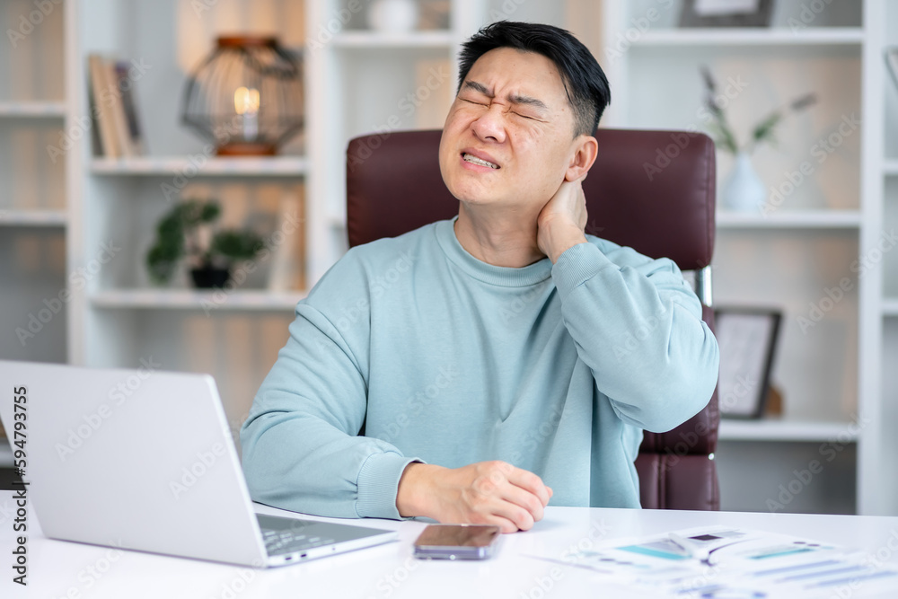 Obraz premium Exhausted young male worker sit at desk massage neck suffer from strain spasm muscles.