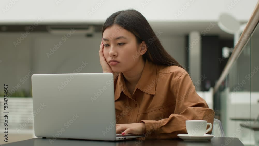 Tired bored Asian businesswoman girl sit in cafe working on laptop sad