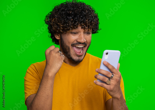 Happy excited joyful indian man in green shirt use smartphone typing browsing shouting say wow yes found out great big win, good news, lottery goal achievemen, celebrating success, winning game