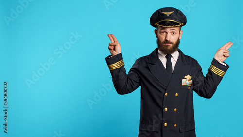 Young serious airliner doing landing signals for planes, helping other pilots to arrive on ground. Aircrew captain showing air gestures with hands on camera, professional occupation.