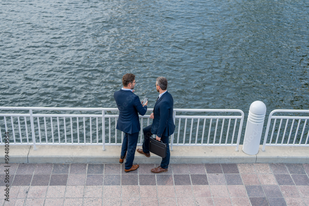 Two business men discussing outdoor during business meeting. Businessmen talking. Brainstorm with serious colleague. Confident business partners walking on street. Business partners talking. Two business men discussing outdoor during business meeting. Businessmen talking. Brainstorm with serious colleague. Confident business partners walking on street. Business partners talking.