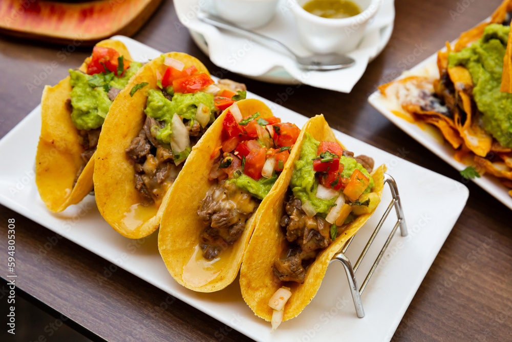 Mexican cuisine. Traditional tacos filled with fried veal, fresh tomatoes and bell pepper, guacamole and salsa