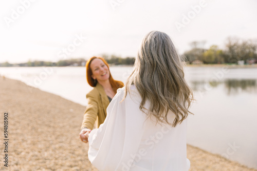 An adult daughter with a gray-haired mother on a walk on the beach, laughing and smiling. Happy old age and care for the elderly